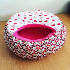 a cat bed with hearts on it sitting on a wooden floor next to a wall