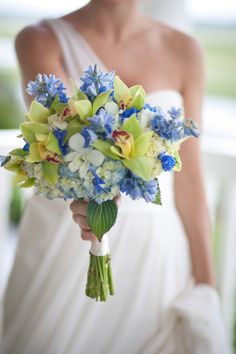 a woman in a white dress holding a bouquet of blue, yellow and white flowers