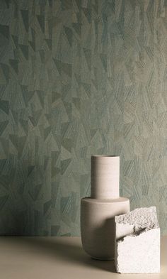 a white vase sitting on top of a table next to a wallpapered background