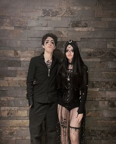 a man and woman dressed up in gothic clothing standing next to each other with their arms around one another