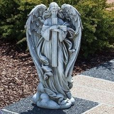 an angel statue sitting on top of a stone slab in front of some bushes and shrubbery