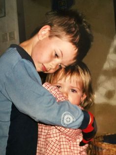 two children hugging each other in front of a wall