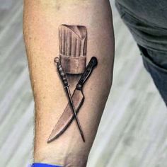 a chef hat and two knives tattoo on the left forearm, with one knife sticking out of it