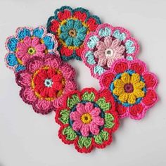 four crocheted flower appliques are shown on a white surface, one is multicolored