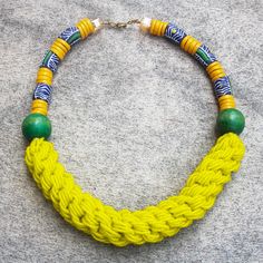 a yellow necklace with green beads on a gray surface and a white beaded chain