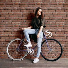 a woman sitting on top of a bike next to a brick wall