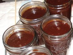 four jars filled with different kinds of food on a table top next to a knife and fork