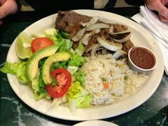 a white plate topped with meat, rice and veggies next to a bowl of sauce