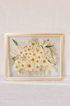 a white and yellow flower arrangement in a gold frame