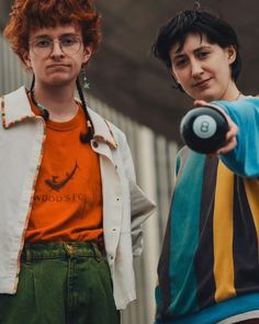 two young men standing next to each other with one pointing at the camera and the other holding an object in his hand