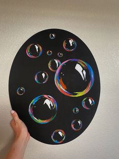 a hand is holding up a black paper plate with bubbles on it and the bottom half has rainbow colors