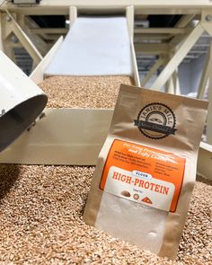 a bag of high protein sits on the ground next to a conveyor belt in a grain mill