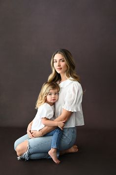 a mother and her daughter sitting on the floor in front of a dark background with their arms around each other