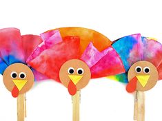 three paper turkeys on wooden sticks with eyes and nose made out of colored tissue paper