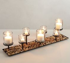 candles are lit on a tray with rocks and pebbles in it, along with some water