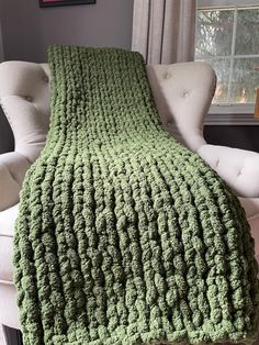 a green crocheted blanket sitting on top of a white chair next to a window