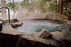 an outdoor hot tub surrounded by rocks and trees