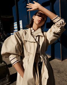 a woman in a trench coat is holding her hands up