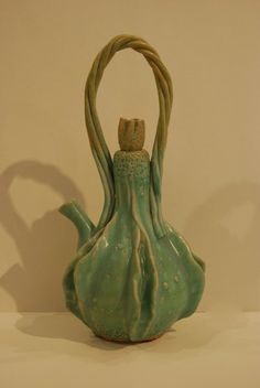 a green ceramic vase with a handle on it's side, sitting on a white surface