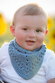 a baby wearing a blue crocheted cowgirl neck scarf in front of sunflowers