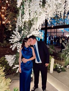 a man and woman standing next to each other in front of a tree with white flowers