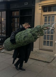 a woman walking down the street carrying a large christmas tree