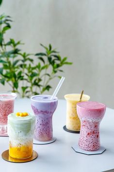 four different colored cups with straws in them sitting on a table next to a potted plant