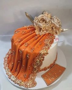 an orange and gold wedding cake with flowers on the top is adorned with golden ribbon