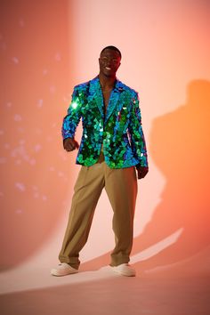 a man standing in front of a pink background wearing a green and blue jacket with sequins on it