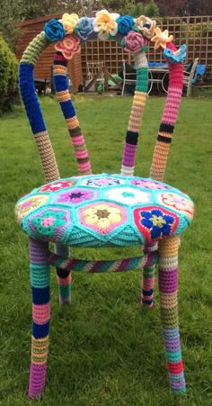 a crocheted chair sitting in the grass with flowers on it's legs