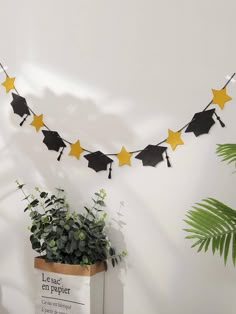 graduation decorations with yellow stars and black caps hanging from a string over a planter