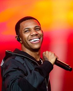 a smiling man holding a microphone in his right hand and wearing a black hoodie