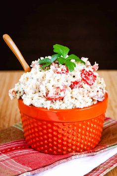 a red bowl filled with rice on top of a wooden table next to a napkin