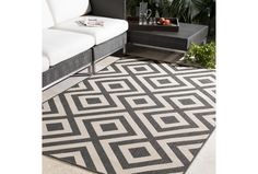 a black and white area rug on the ground near a couch, coffee table and potted plant