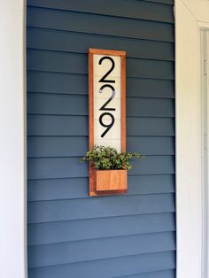 a house number sign mounted to the side of a blue wall with a planter