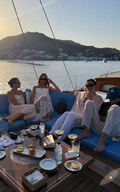 three people sitting on a boat with food and drinks in front of them, while the sun is setting