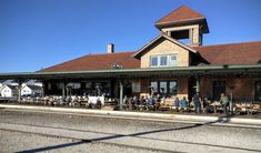 people sitting at tables in front of a train station