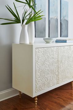 a white cabinet with two vases and a plant in it on top of a hard wood floor