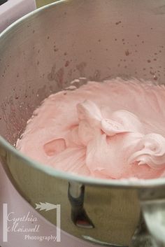 a metal bowl filled with pink icing on top of a counter