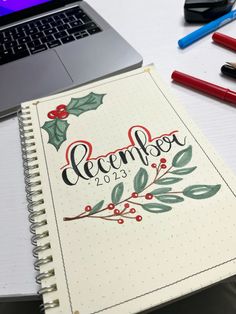 a notebook with the word december written on it next to a laptop computer and pens