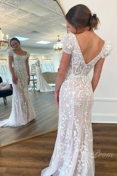 a woman in a wedding dress looking at herself in the mirror with her back to the camera