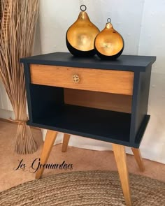 two golden vases sitting on top of a black and wooden table next to a plant