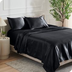 a bed with black sheets and pillows in a room next to a lamp on a table