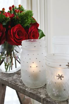 some red roses are sitting on a table next to two glass jars with candles in them