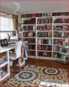 a room filled with lots of books on top of a white book shelf next to a desk