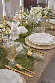 the table is set with gold and white plates, silverware, napkins, and bunny figurines