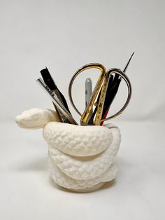 a white vase with scissors, pens and other items in it on a white surface