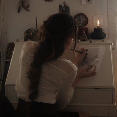 a woman sitting at a desk writing on a piece of paper in front of a clock