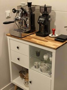 a coffee maker sitting on top of a wooden counter next to a white cabinet filled with cups