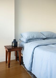 a bed with blue sheets and pillows next to a night stand on the floor in front of a white wall